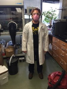 A man in a lab coat and mask in front of a glove box